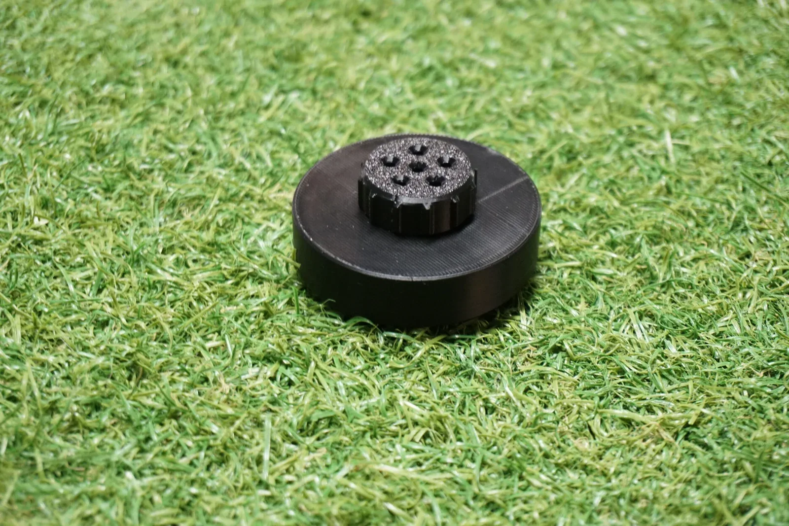 Black scent container with six holes lying on artificial turf