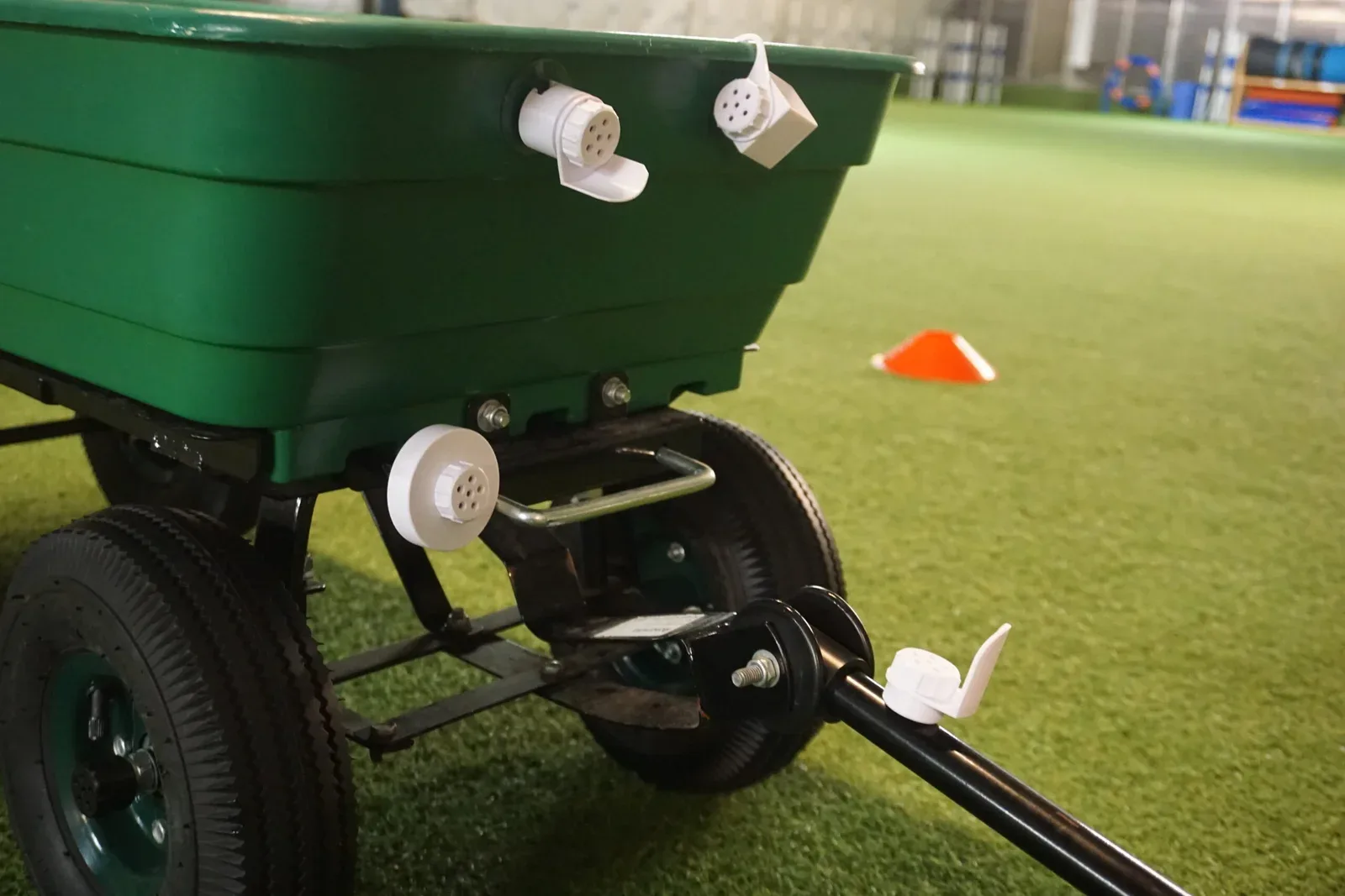 Green garden wagon on artificial turf with three white scent containers attached to the rim and frame