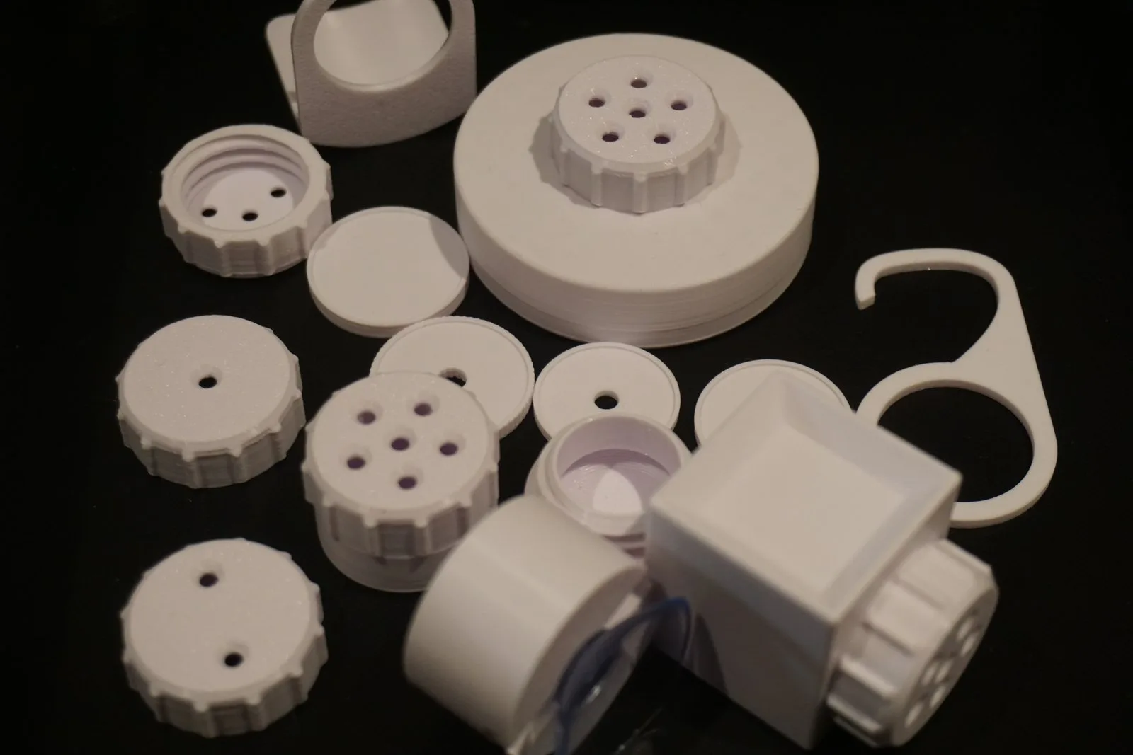 All the parts in white PLA on a black background: containers, lids with different numbers of holes, shelf mount, and hook